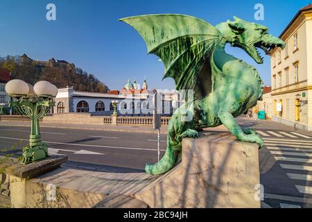 Dragon statue on Dragon bridge and Ljubljana castle and Saint Nicholas Cathedral in the background, Ljubljana, Slovenia Stock Photo