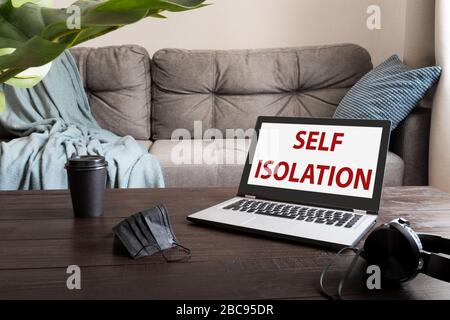 Remote office at home. Laptop, medical mask and cup of coffee on wooden table. Quarantine. Text - Self isolation. Stock Photo