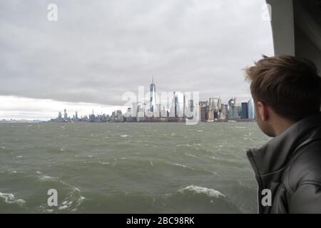 Man looking toward Manhattan skyline from the water looking toward Battery Park Stock Photo