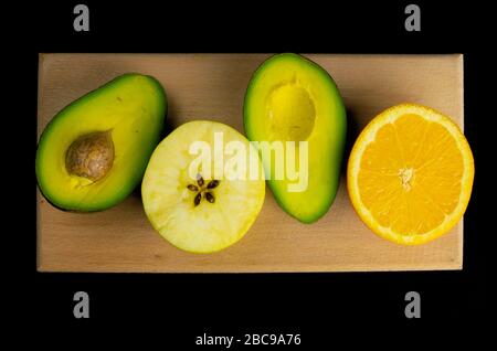 The concept of healthy diet and vegetarianism. Sliced avocado, apple and orange on a wooden board isolated on black background. Flat lay food Stock Photo