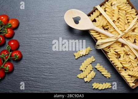 Background and space for text with a cardboard box of raw spiral pasta photographed from above, on a gray slate board and a bow made of bast and a woo Stock Photo