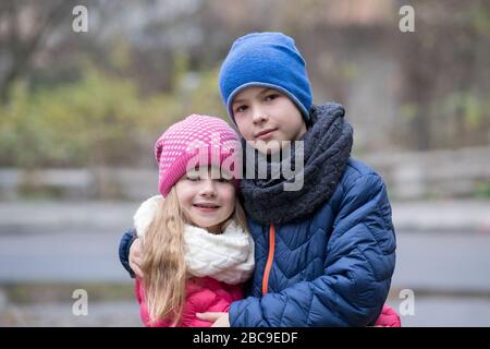 Two children boy and girl hugging each other outdoors wearing warm clothes in cold autumn or winter weather. Stock Photo