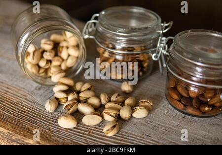 Pistachios scattered on the white vintage table from a jar and with other nuts on background. Pistachio is a healthy vegetarian protein nutritious Stock Photo