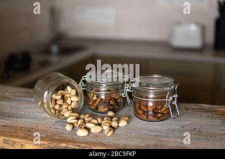 Pistachios scattered on the white vintage table from a jar and with other nuts on background. Pistachio is a healthy vegetarian protein nutritious Stock Photo
