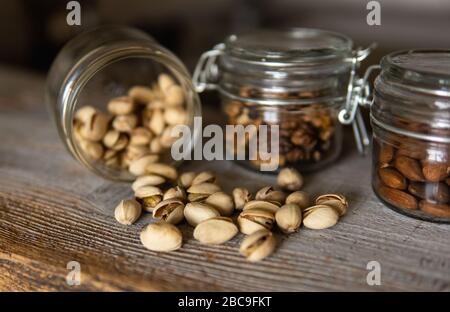 Pistachios scattered on the white vintage table from a jar and with other nuts on background. Pistachio is a healthy vegetarian protein nutritious Stock Photo