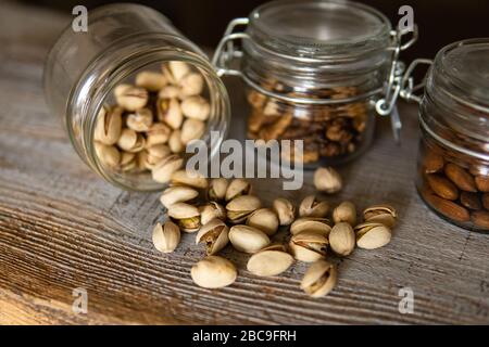 Pistachios scattered on the white vintage table from a jar and with other nuts on background. Pistachio is a healthy vegetarian protein nutritious Stock Photo