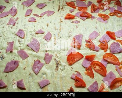 Mayonnaise dough divided into two parts with slices of ham on one half and slices of ham with tomatoes on other half Stock Photo