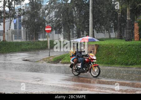 A roofed taxi motorcycle carries a woman in rain on a macadamized road in Rwamagana, Rwanda Stock Photo