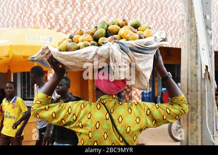 Woman sells ripe mango fruits on a basket in a busy place in Rwamagana town, Rwanda, East Africa Stock Photo