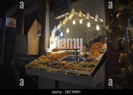 A tired male stallholder sits amid his attractive and beautifully lit olive display at a stall in Marrakech medina, Morocco. Stock Photo