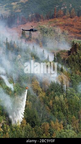 helicopter drops stream on water on Alaskan forest fire Stock Photo