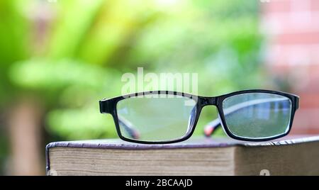 Stack of books with reading glasses on top. Green nature background. Home school or study concept. Copy space. Stock Photo