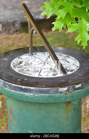Vintage brass sun clock on green cast metal cylindrical post. Stock Photo