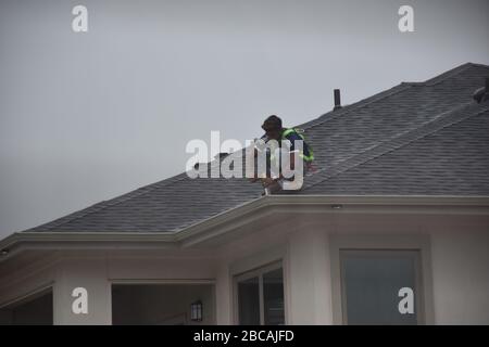 A man contractor worker on roof top working on a cloudy rainy day.standing sitting walking kneeling. fixing roof.rain water system gutter fixing on kn Stock Photo