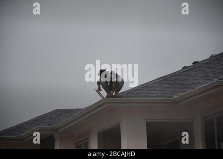 A man contractor worker on roof top working on a cloudy rainy day.standing sitting walking kneeling. fixing roof.rain water system gutter fixing on kn Stock Photo