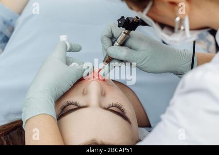 Woman having permanent makeup on lips in beauty salon. Cosmetologist in gloves applying tattoo with machine, macro view Stock Photo