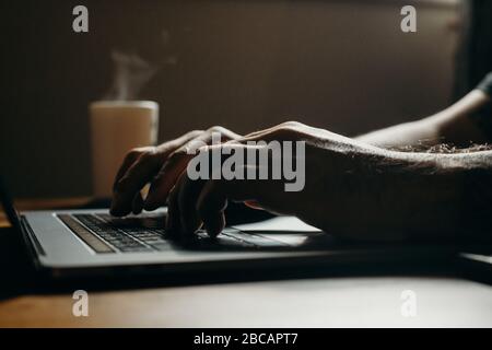 Side view closeup shot of man using laptop in dark area. Working overtime with a coffee. Stock Photo