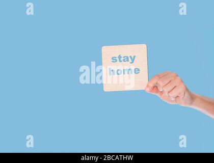 Hand holding a wooden blank with stay home on blue background Stock Photo