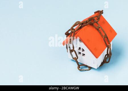 Toy house wrapped in a chain on a blue background with copy space. Property arrest concept Stock Photo