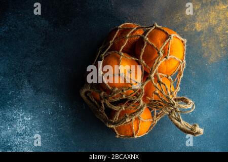 Ripe organic oranges in string bag on dark wooden background as a healthy and recycling concept Stock Photo