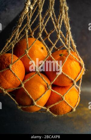 Ripe organic oranges in string bag on dark wooden background as a healthy and recycling concept Stock Photo