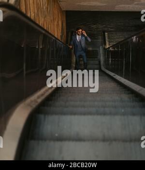 Businessman going up on the escalator while holding sunglasses on a sunny day Stock Photo