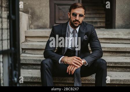 Serious businessman sitting on the stairs and holding his watch while looking in to a camera Stock Photo