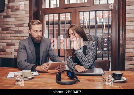 Team of two business colleagues  working together discussing new project using tablet, while sitting in cafe. Stock Photo
