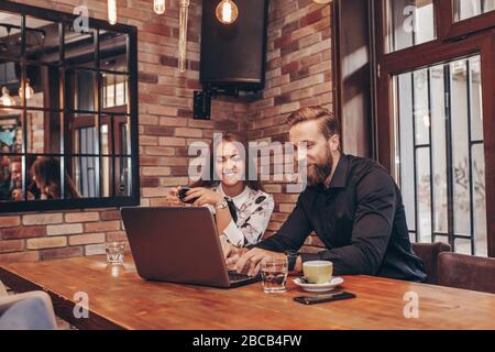 Business couple having discussion about job, while sitting in cafe and using laptop computer. Stock Photo