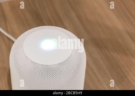 White Apple HomePod on a table with Siri light lit on top. Stock Photo