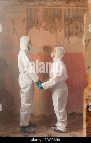 Couple of virologist doctors and scientists wearing biohazard protective suits and holding hands full of hope after a nuclear core meltdown disaster Stock Photo