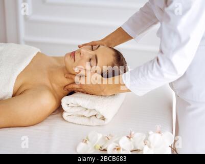 Beautiful brunette woman enjoying facial massage with closed eyes. Relaxing treatment in medicine and spa center concepts Stock Photo