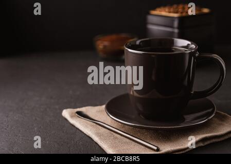 A black coffee Cup, metal jar of roasted coffee beans on a dark concrete table Stock Photo
