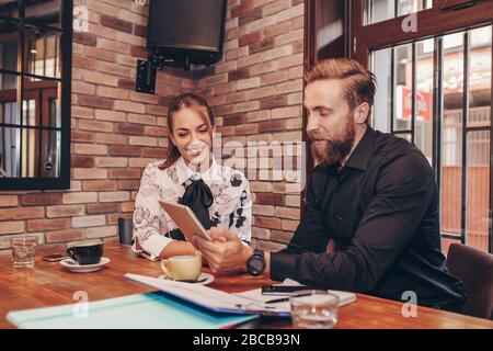 Team of two business colleagues  working together discussing new project using tablet, while sitting in cafe. Stock Photo