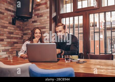 Two young positive business people having a successful meeting while working together in a cafe with laptop. Stock Photo