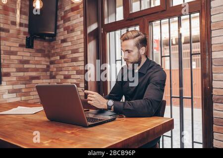 Young successful businessman texting on smart phone and  working on a laptop while sitting in cafe. Stock Photo