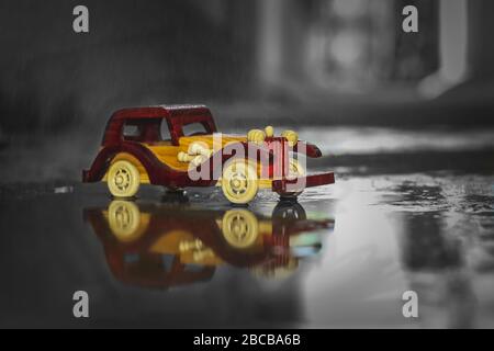Reflection Vintage toy car under the rain on the road. Miniature Car Toy reflection in Rain. Reflection Red and yellow vintage car on rain. Rain falli Stock Photo