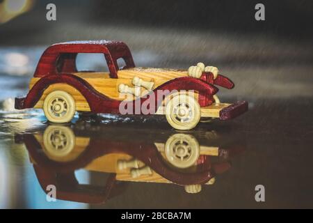 Reflection Vintage toy car under the rain on the road. Miniature Car Toy reflection in Rain. Reflection Red and yellow vintage car on rain. Rain falli Stock Photo