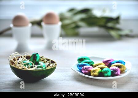small chocolate eggs in colored wrapper on saucer, two eggs in stands in the background in blur Stock Photo