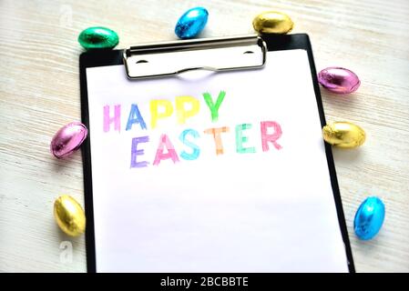 The inscription of a happy Easter on a white sheet surrounded by small chocolate eggs Stock Photo