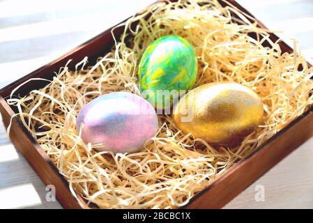 Three colored chicken eggs in a box with shavings in the sunlight Stock Photo