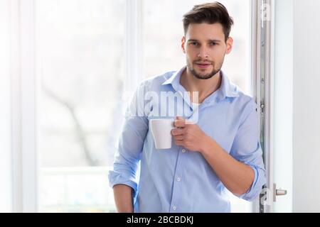 Man drinking cup of coffee near window Stock Photo
