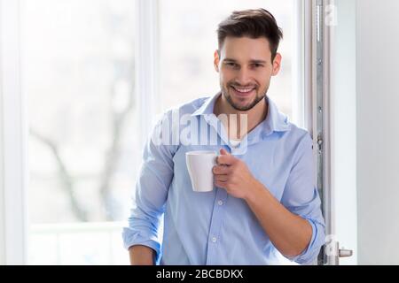 Man drinking cup of coffee near window Stock Photo