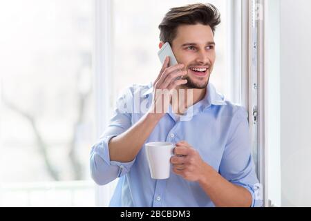 Man drinking cup of coffee near window Stock Photo