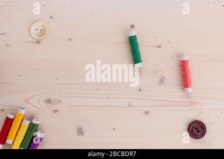 Buttons and spools with different color of thread for sewing lying on a wooden background. Set for needlework top view Stock Photo