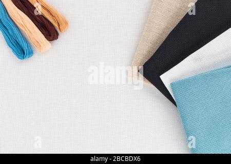 Different color of thread for sewing and canvas for embroidery lying on a white background. Set for needlework top view Stock Photo