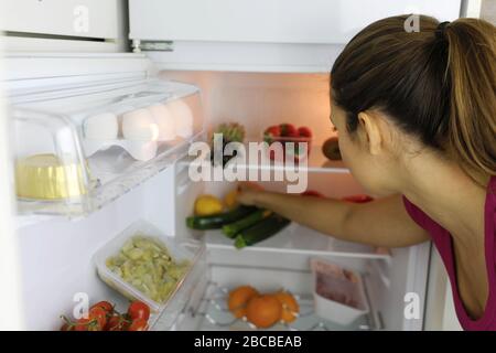 Back view of young woman searching for healthy food in the fridge Stock Photo