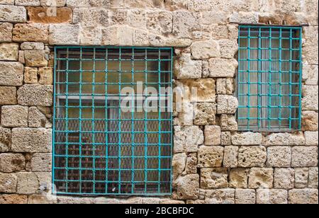Barred windows in an old, dilapidated porous sandstone wall Stock Photo