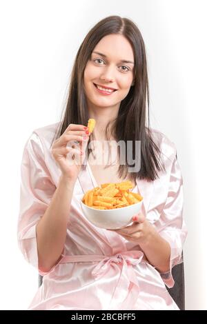 Attractive young brunette woman wearing a pink nightgown, eating potato chips smiling. Royalty free stock photo. Stock Photo