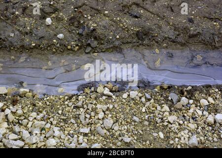 frozen puddle on dirt road in late winter, rural scene with frozen puddle between car tracks in wet soil and pebbles close-up Stock Photo